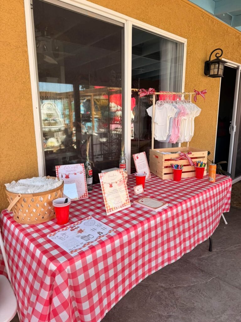 Welcome table with red gingham, a baby clothes line, a basket and guest cards