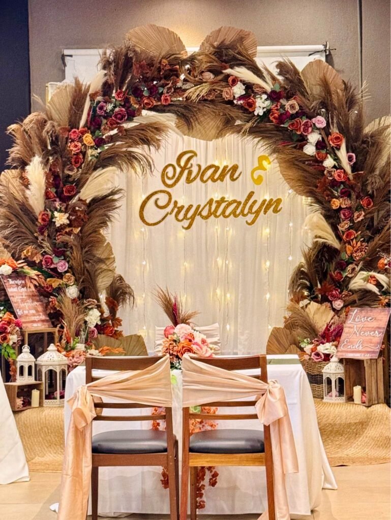 Rustic wedding backdrop with a round pampas grass and dried flower arch, gold name sign and sweetheart table