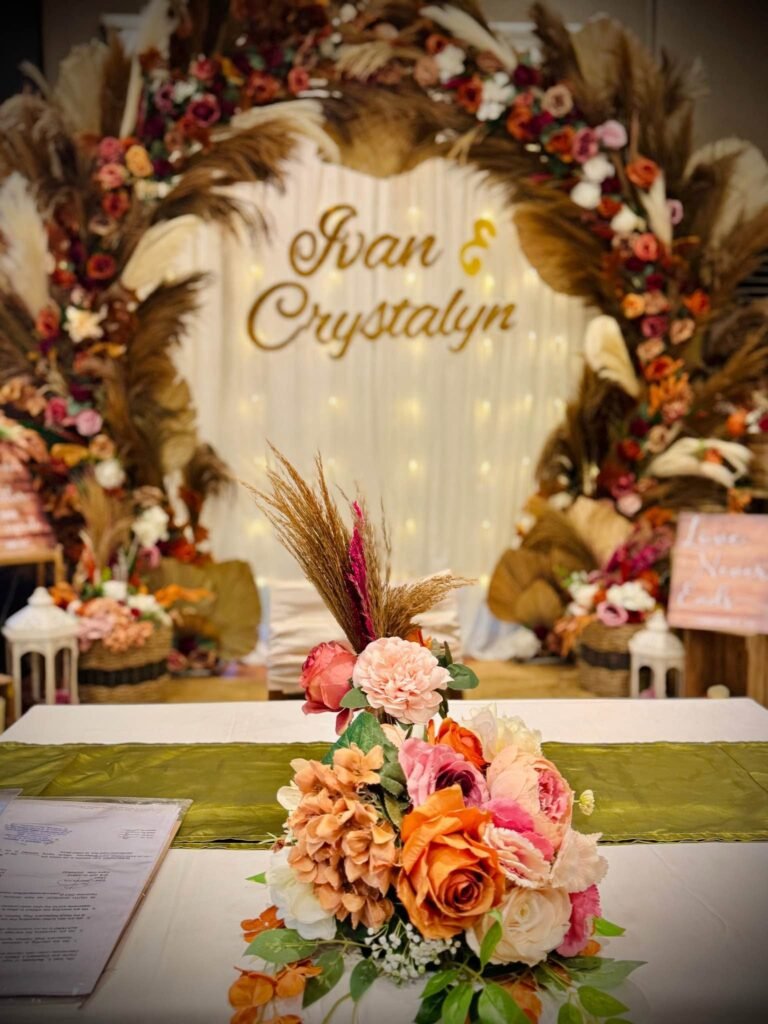 Close up of a gold script name sign in front of fairy lights inside a pampas and rose arch