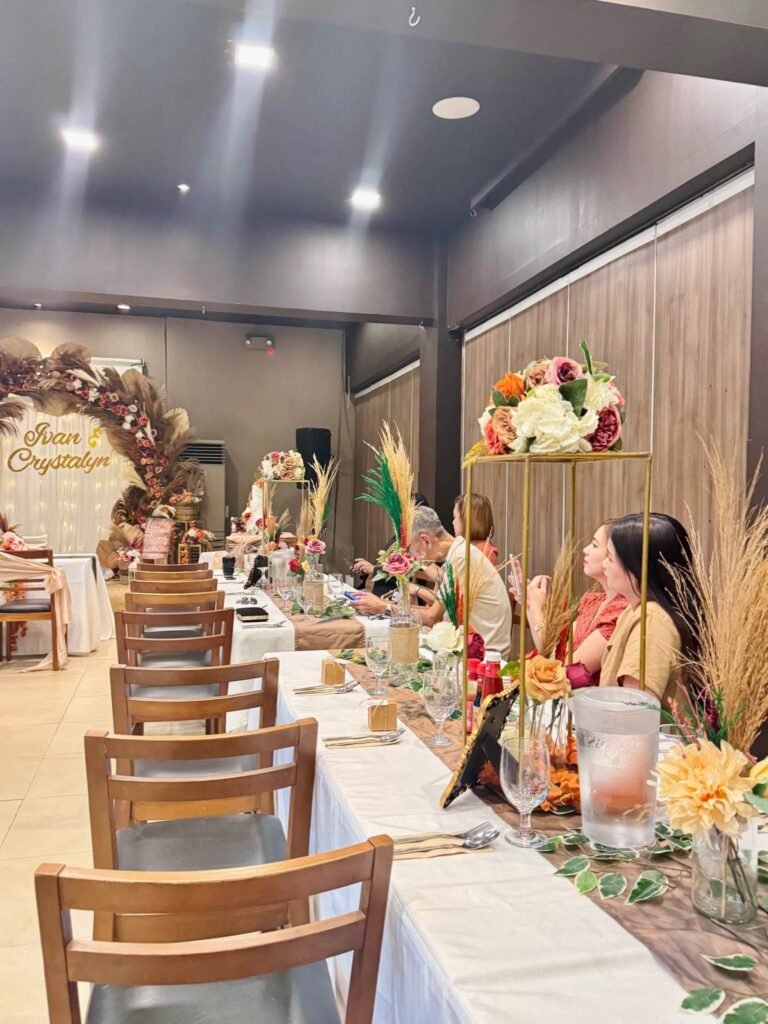 Long rustic wedding reception tables with wood chairs, pampas centerpieces and the floral arch at the end