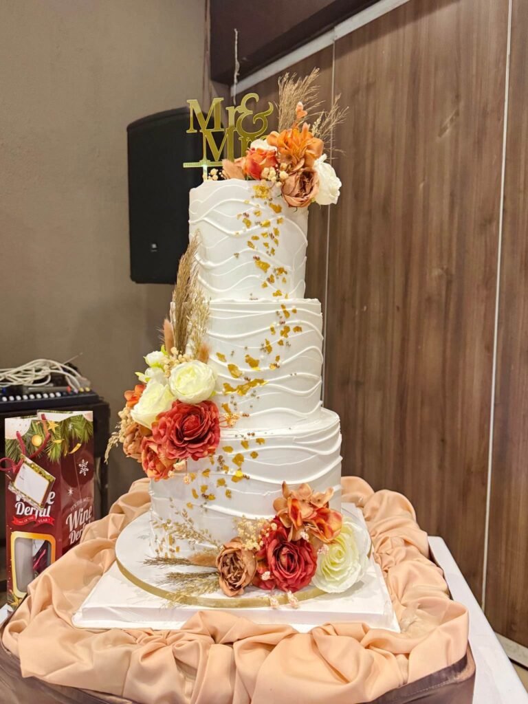 Four tier white wedding cake with burnt orange roses, pampas and a gold Mr and Mrs topper