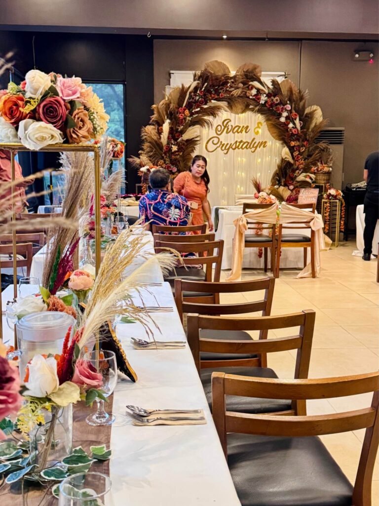 Guests at a rustic wedding reception table with pampas centerpieces and the floral arch behind