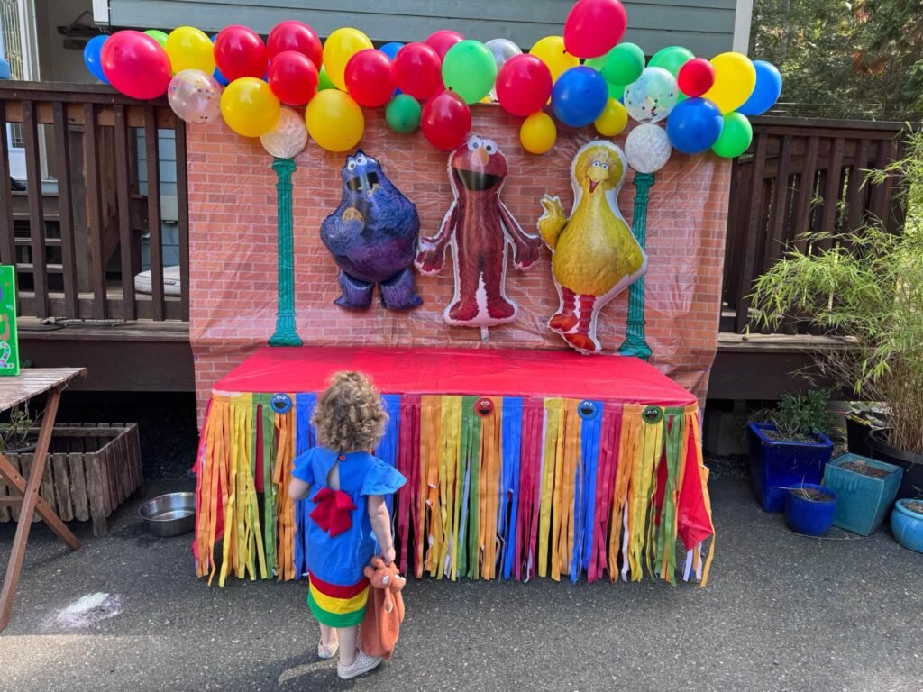 Sesame Street party table with a rainbow balloon garland, fringe skirt and character figures