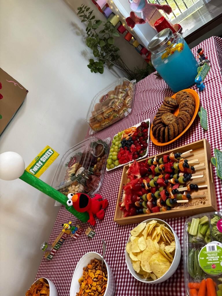Sesame Street snack table with red gingham, Elmo figure, fruit skewers and chips
