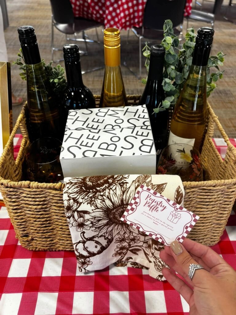 Wicker gift basket with wine bottles, a floral tea towel and a gift box as a baby shower prize