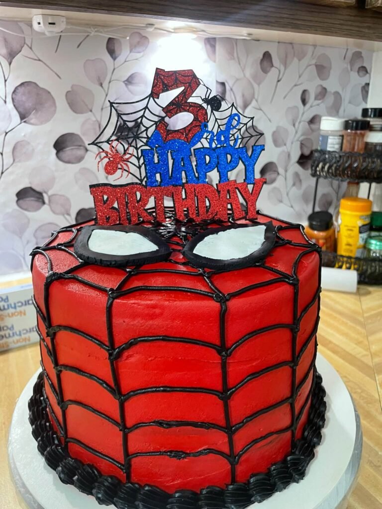 Side view of a red Spiderman cake with web piping and black shell border