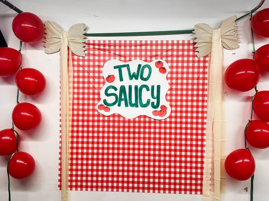 Two Saucy birthday sign on a red gingham backdrop with red balloons