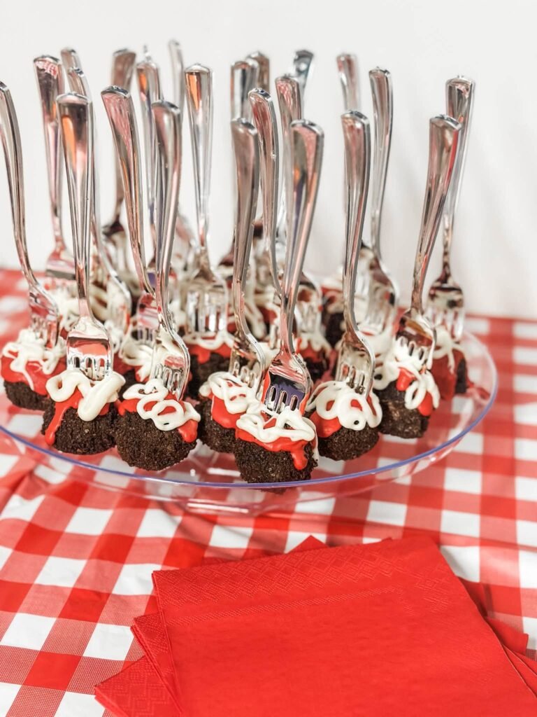 Brownie meatball bites on forks with red sauce on a red gingham table