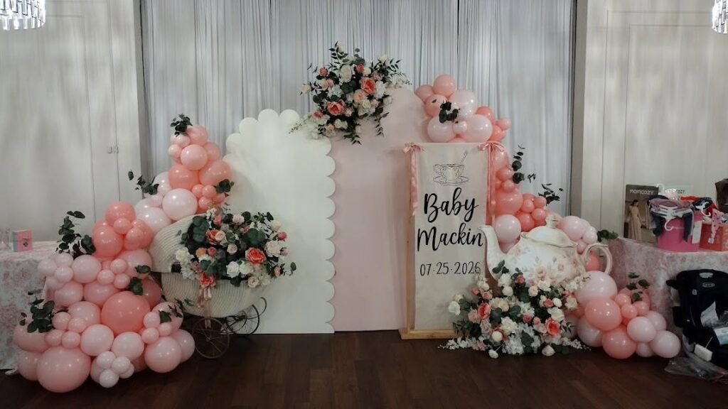 Tea party baby shower backdrop with pink balloons, flowers, scalloped panels and a name sign