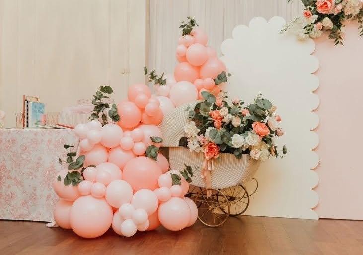 Pink balloons and flowers around a vintage pram in front of a scalloped panel