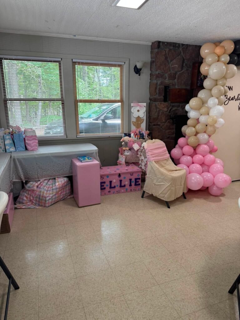 Teddy bear baby shower room with a balloon garland, pink seating and a gift area