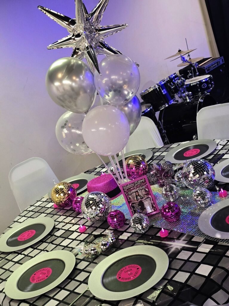 Disco table with record plates, silver starburst balloons and a mirror ball centerpiece