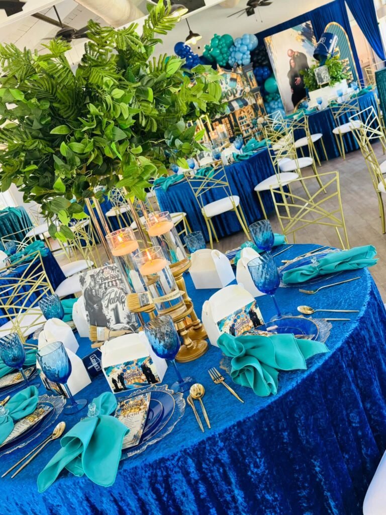Round baby shower table with greenery centerpiece, teal napkins and gold cutlery