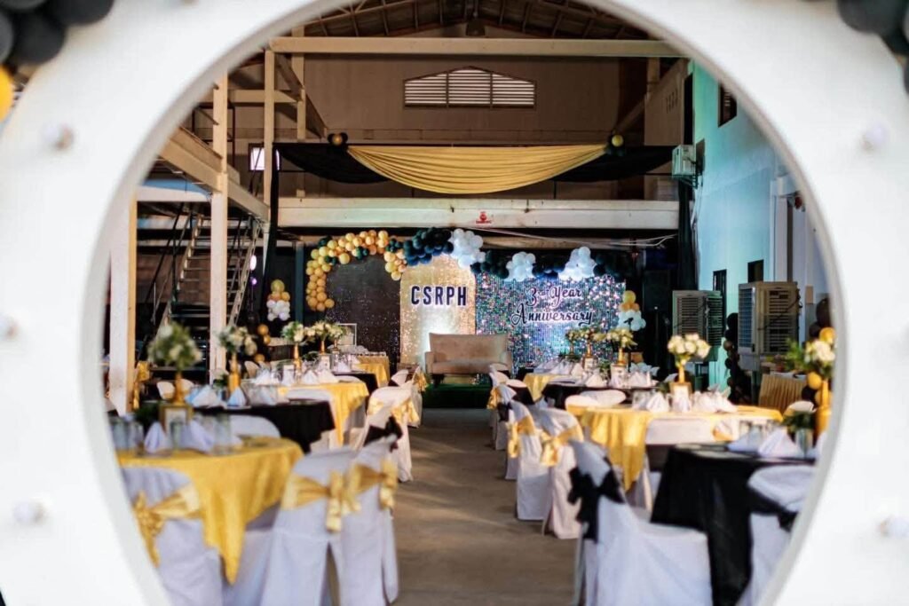Reception hall with round tables in black and gold linens and white chairs with sashes