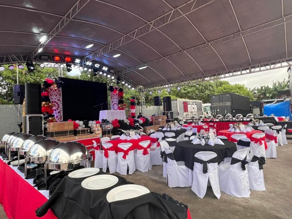 Outdoor tent reception with red and black tables, white chair covers and a buffet line of chafing dishes