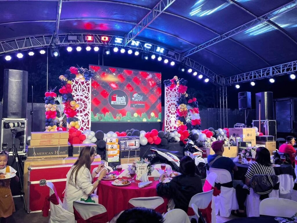 Reception stage with a red and white floral backdrop, lights and guest tables in front