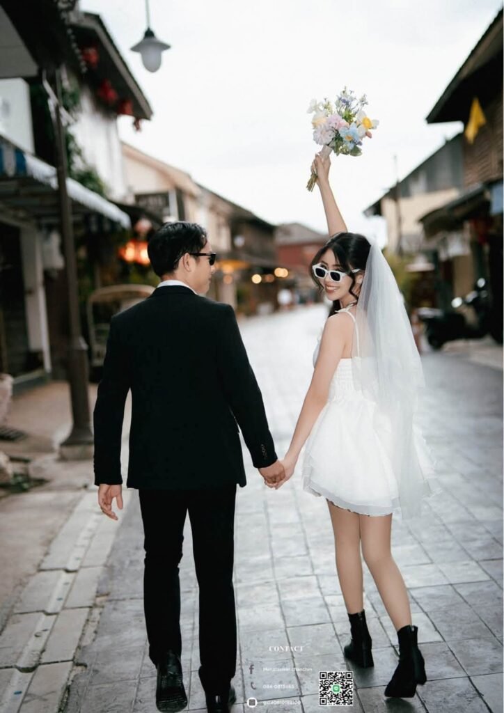 Couple walking hand in hand down an old city street, bride in a short white dress and veil holding a bouquet up