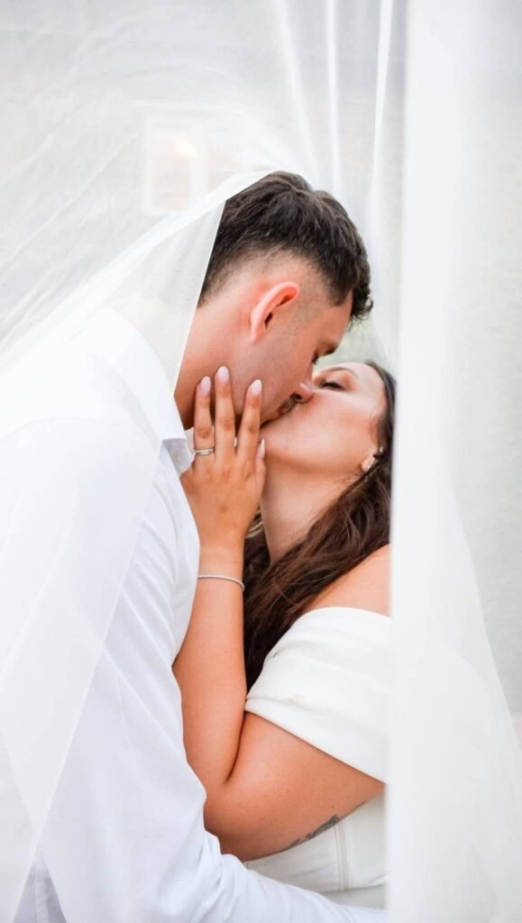 Couple kissing behind a sheer veil in soft light