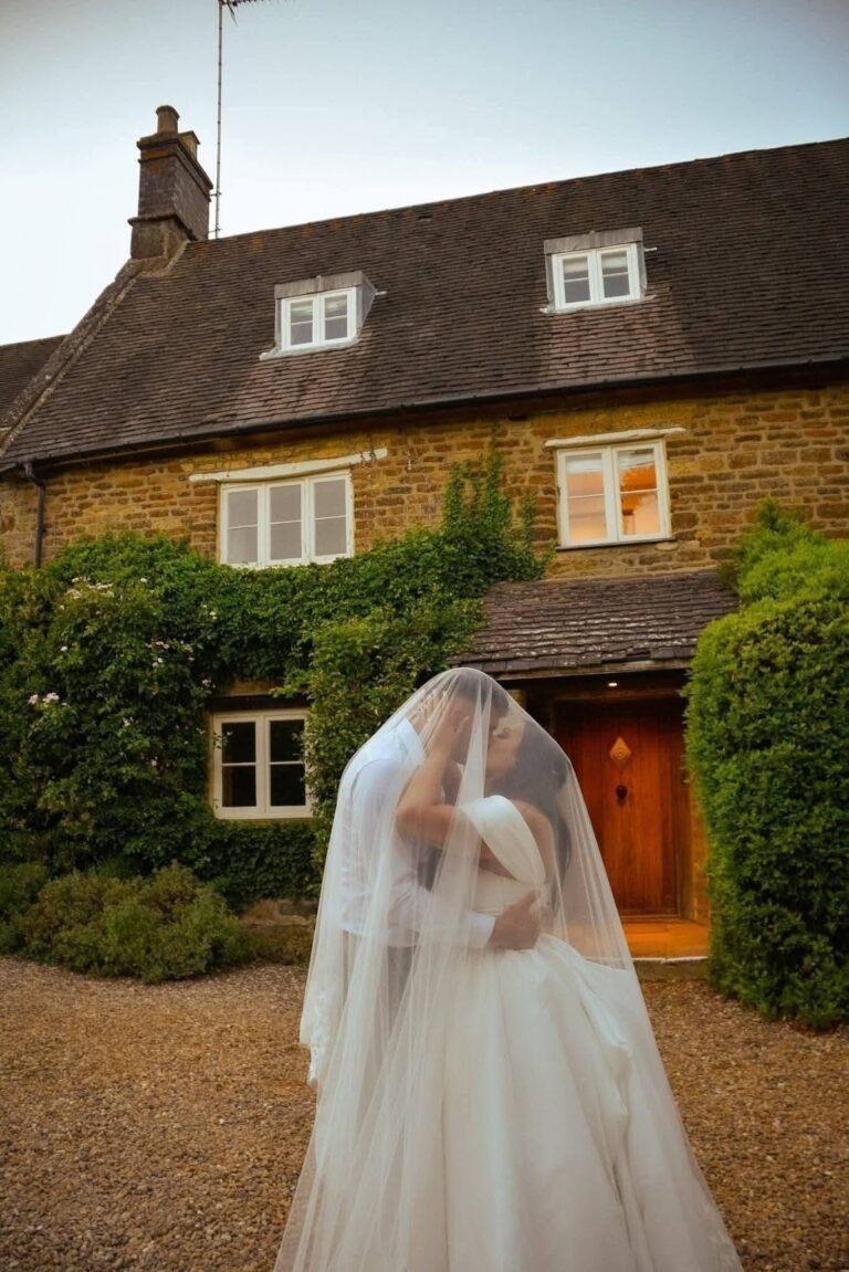 Couple under the bridal veil in front of an old stone cottage