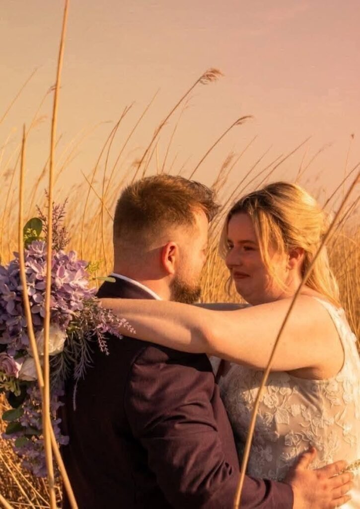 Couple hugging in tall grass at sunset with a lavender bouquet