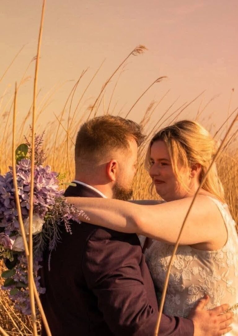 Couple hugging in tall grass at sunset with a lavender bouquet