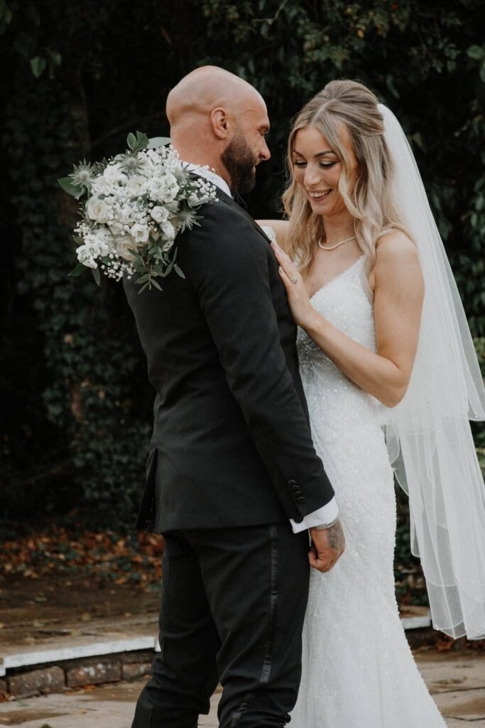 Bride and groom smiling at each other in a garden with a baby breath bouquet
