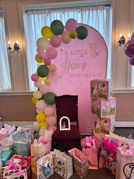 Winnie the Pooh baby shower backdrop with a mom to be chair, BABY blocks and a pile of pink gift bags