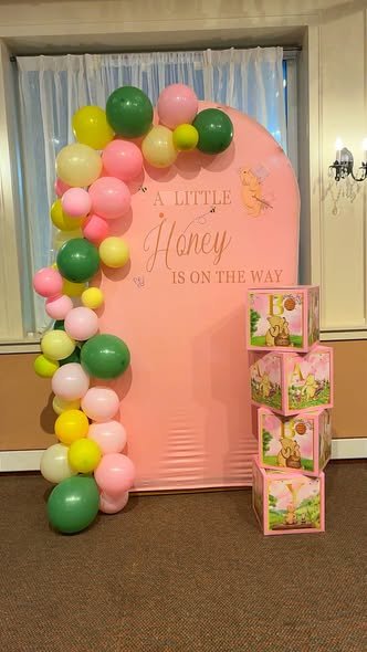 Pink Winnie the Pooh baby shower backdrop with an A Little Honey Is on the Way arch, BABY blocks and a pink, yellow and green balloon garland