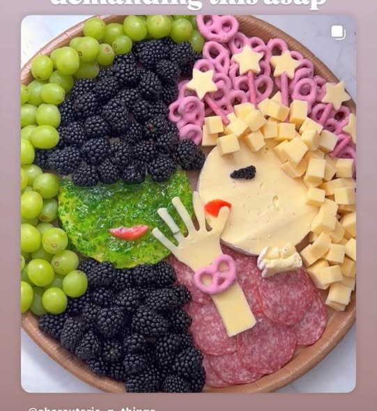 Snack board shaped like Elphaba and Glinda made with grapes, blackberries, cheese, salami and pink pretzels