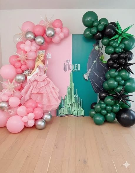 Wicked party backdrop with pink and silver balloons, a Glinda cutout, an Emerald City panel and green and black balloons