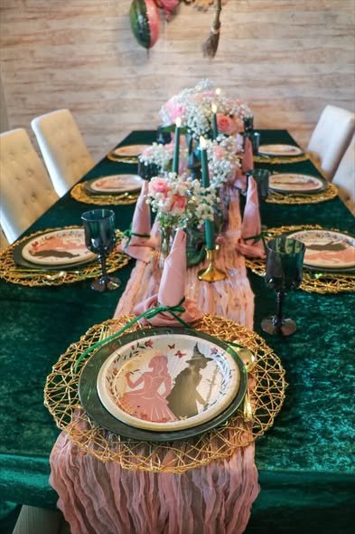 Wicked party table with a green velvet tablecloth, pink gauze runner, gold woven chargers and green goblets