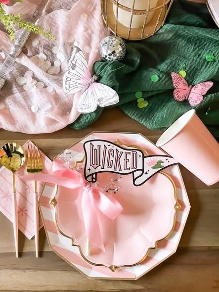 Pink Wicked place setting with a gold rim plate, pink bow, Wicked pennant, butterflies and gold cutlery