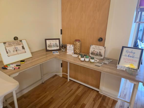 Baby shower games table with woodland signs, a guest book frame and supplies along a wall