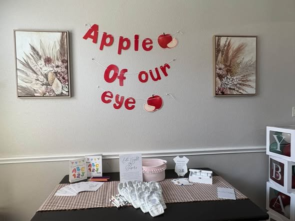 Red Apple of Our Eye letters on a wall above a baby shower table
