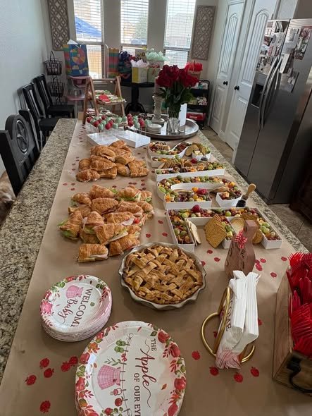 Long baby shower food spread with croissant sandwiches, pies and floral plates