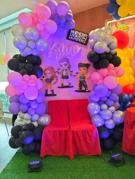 Purple, lilac and black balloon arch with character cutouts and a red chair
