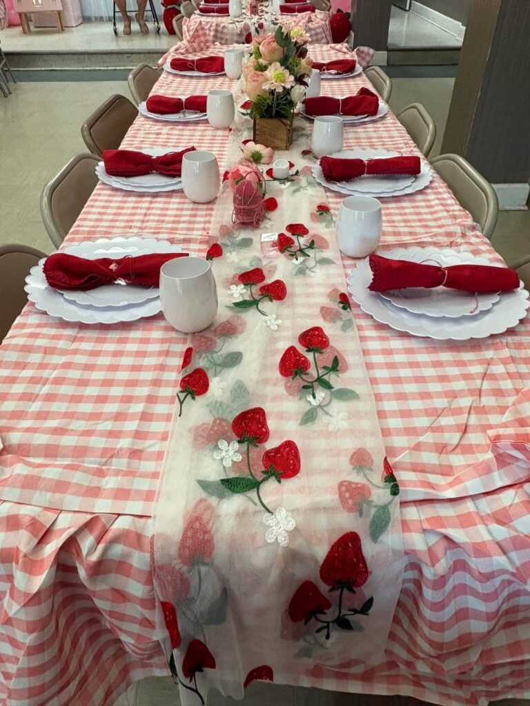 Long baby shower table with pink gingham cloth, a strawberry runner and red napkins
