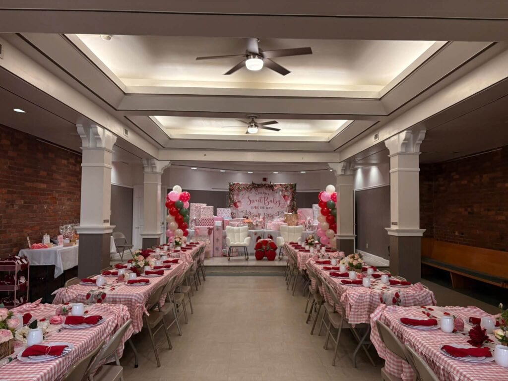 Wide view of a baby shower hall with pink and white tables in rows