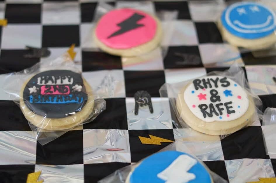 Custom sugar cookies with lightning bolts, smiley faces and the twins names on a checkered cloth