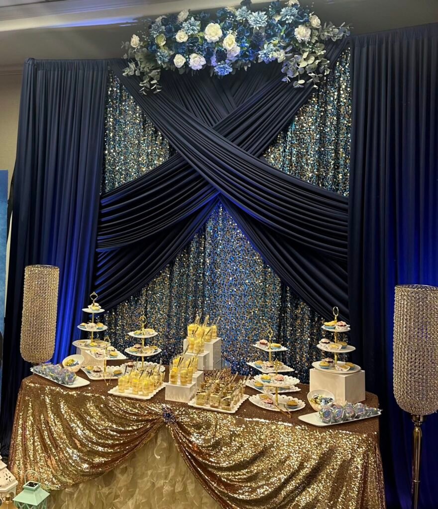 Navy drape graduation backdrop with flowers over a gold sequin dessert table