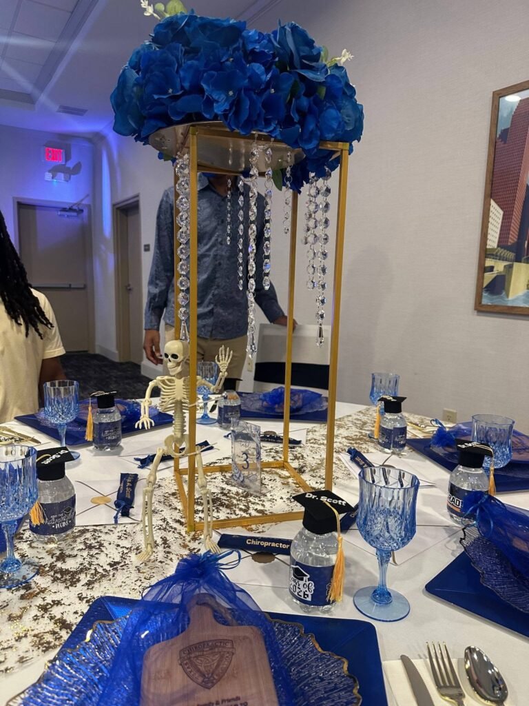 Tall gold centerpiece with blue roses and crystals on a graduation table