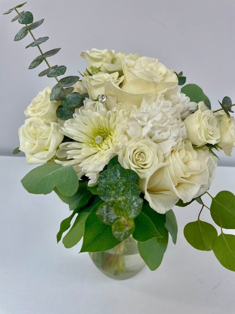 White flower centerpiece in a round glass vase with eucalyptus