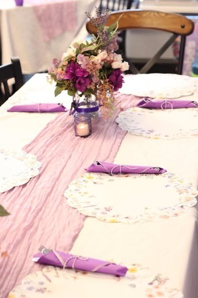 Long baby shower table with lilac runner, doilies and purple napkins