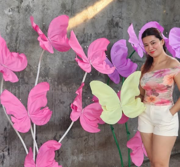 Woman posing with giant pink and yellow paper butterfly stands