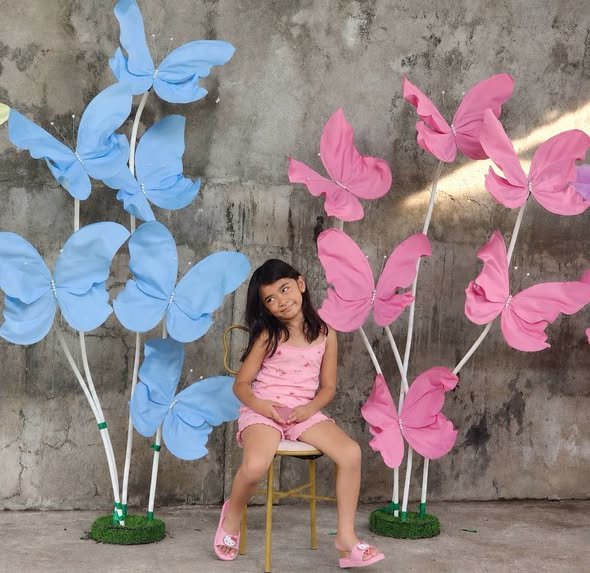 Girl sitting on a stool in front of giant blue and pink paper butterflies