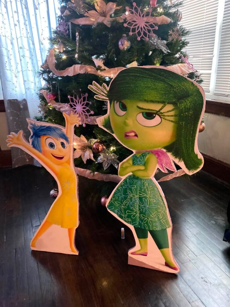 Tall Joy and Disgust Inside Out cutouts next to a pink Christmas tree