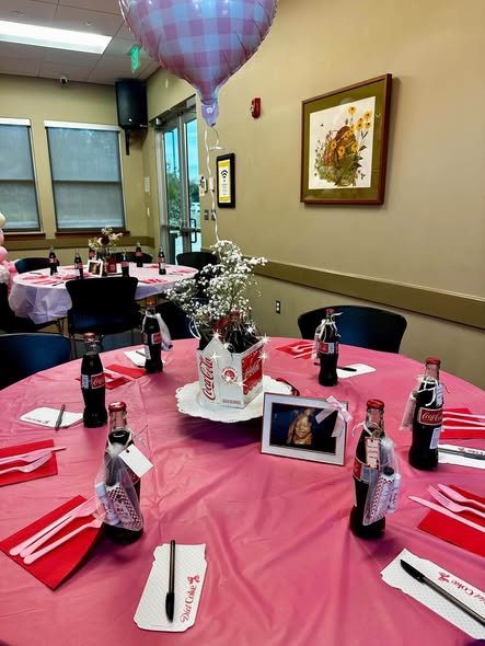 Round baby shower tables with pink cloths, red stripes and soda bottle centerpieces