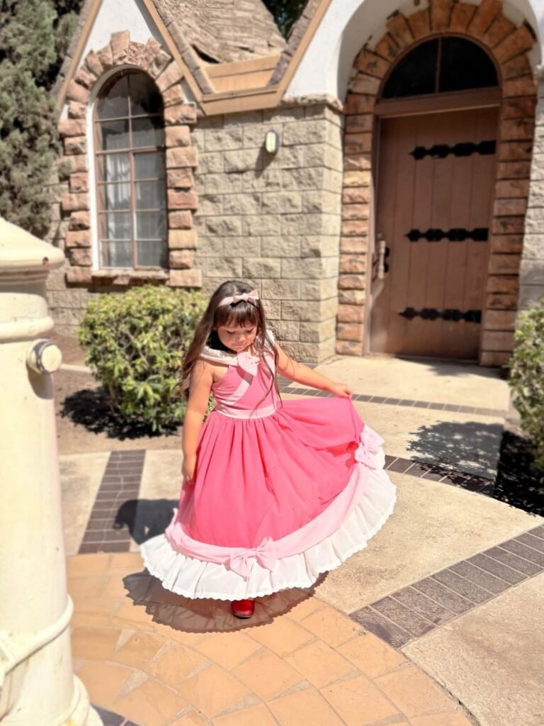 Birthday girl in a pink princess dress twirling in front of a stone house
