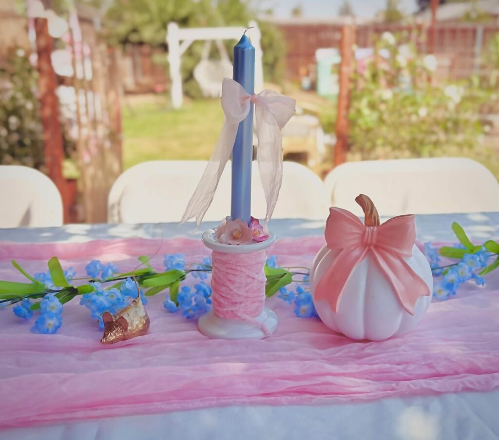 Blue taper candle, pink ribbon and a pink pumpkin on a pink table runner