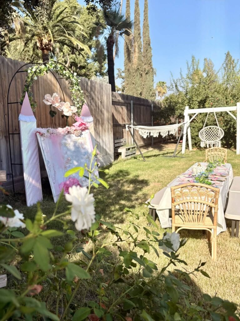 Outdoor Cinderella party with a castle backdrop, wicker chairs and a long table in a garden